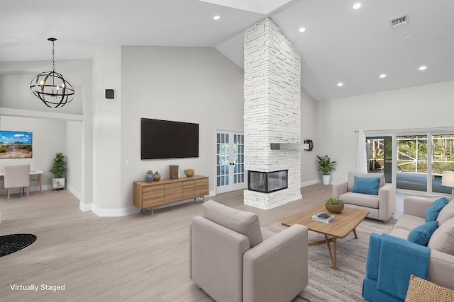 living area with high vaulted ceiling, a notable chandelier, a fireplace, visible vents, and light wood-style floors