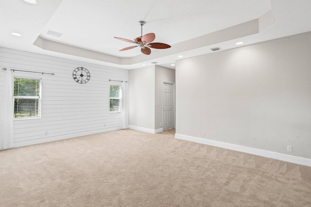 empty room with plenty of natural light, a raised ceiling, and light colored carpet