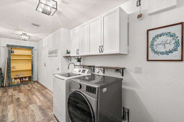 laundry room featuring cabinet space, visible vents, light wood-style floors, washing machine and dryer, and a textured ceiling