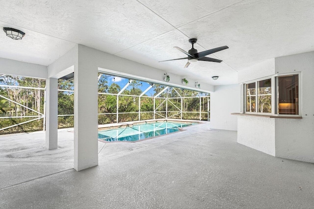 pool with glass enclosure, ceiling fan, and a patio