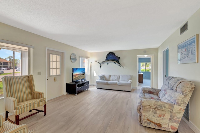 living room with visible vents, plenty of natural light, a textured ceiling, and light wood finished floors