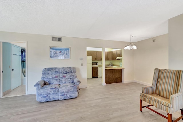 sitting room with a textured ceiling, visible vents, baseboards, light wood finished floors, and an inviting chandelier