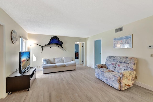 living area with visible vents, light wood-style flooring, baseboards, and a textured ceiling