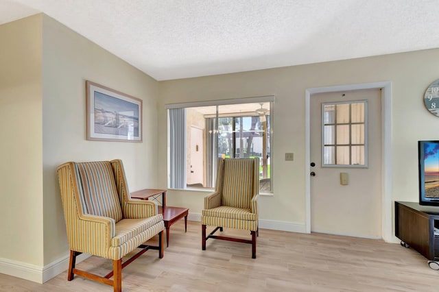 living area with a textured ceiling, light wood-style flooring, and baseboards