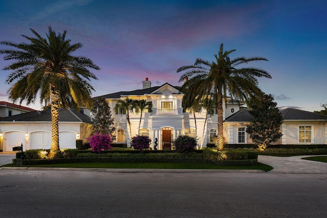 view of front of home featuring an attached garage, a chimney, driveway, and stucco siding