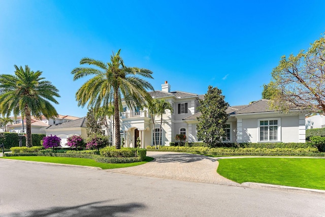 view of front facade with a balcony, stucco siding, a front lawn, a tiled roof, and decorative driveway