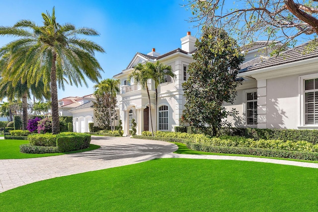 view of front of home with a chimney, stucco siding, curved driveway, and a front lawn