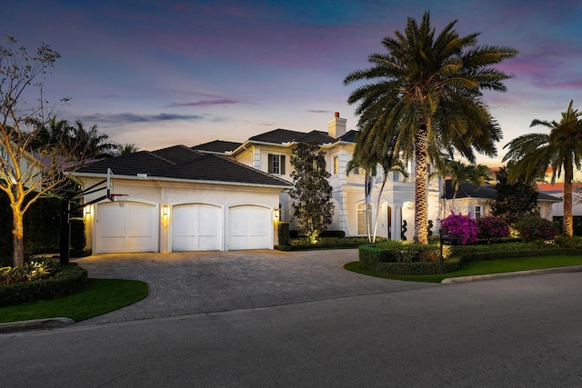 view of front facade featuring an attached garage, a chimney, stucco siding, a tiled roof, and decorative driveway