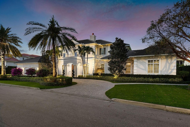 view of front of house with a front lawn, curved driveway, a chimney, and stucco siding