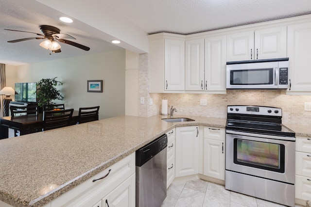 kitchen with a textured ceiling, a peninsula, a sink, appliances with stainless steel finishes, and backsplash