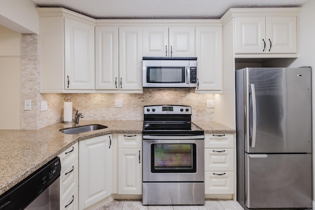 kitchen featuring light stone counters, light tile patterned flooring, a sink, appliances with stainless steel finishes, and tasteful backsplash