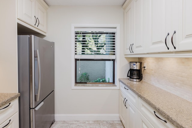 kitchen with tasteful backsplash, baseboards, white cabinets, freestanding refrigerator, and light stone countertops