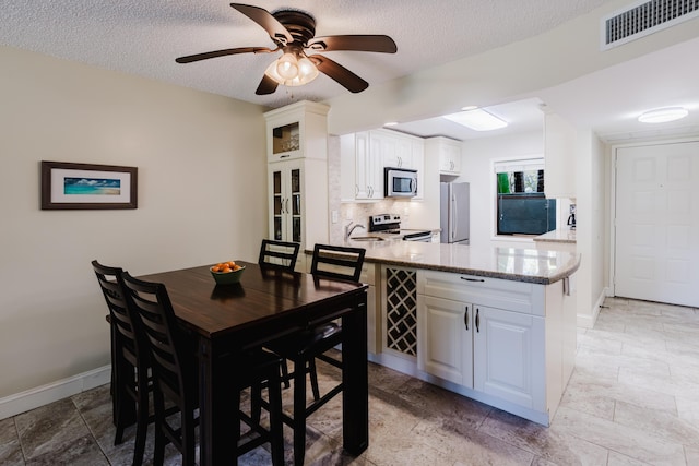 dining area featuring a ceiling fan, visible vents, a textured ceiling, and baseboards