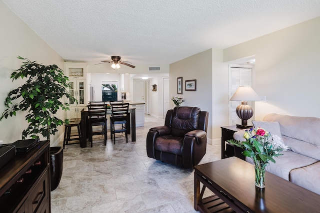 living room featuring a textured ceiling, baseboards, visible vents, and a ceiling fan