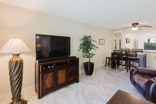 living room featuring ceiling fan, baseboards, and a textured ceiling