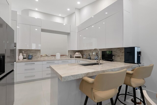 kitchen with white cabinets, modern cabinets, a peninsula, a kitchen bar, and a sink