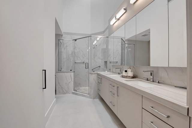 full bath featuring double vanity, a marble finish shower, backsplash, and a sink