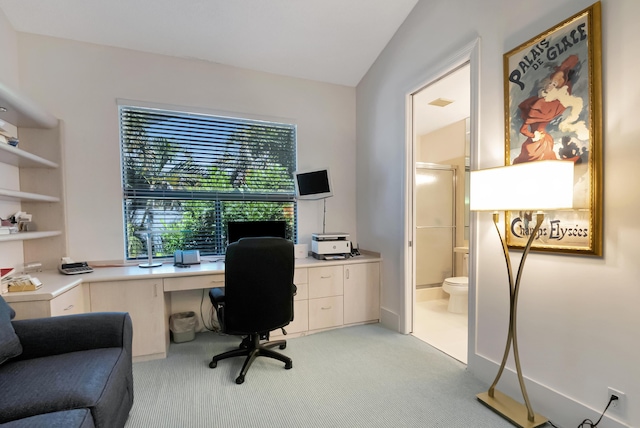 home office featuring lofted ceiling, light carpet, and built in desk