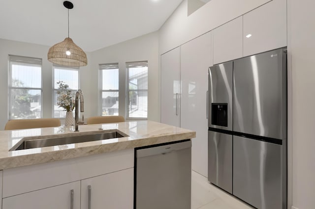 kitchen with light stone counters, decorative light fixtures, appliances with stainless steel finishes, white cabinets, and a sink