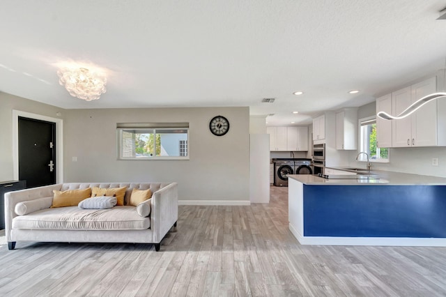 living room featuring visible vents, a notable chandelier, light wood-style flooring, washing machine and dryer, and baseboards
