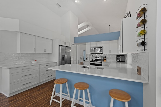 kitchen featuring dark wood finished floors, appliances with stainless steel finishes, white cabinets, a peninsula, and a kitchen bar