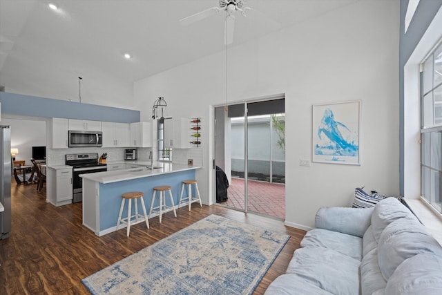 kitchen with high vaulted ceiling, stainless steel appliances, a peninsula, white cabinets, and a kitchen breakfast bar