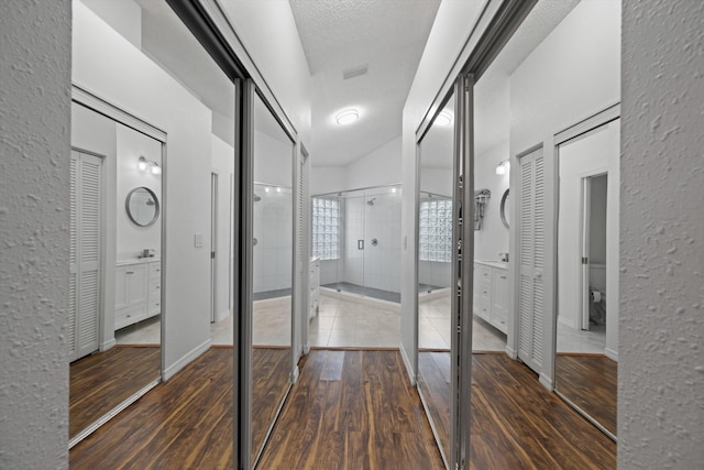 corridor featuring a textured ceiling, a textured wall, wood finished floors, visible vents, and baseboards