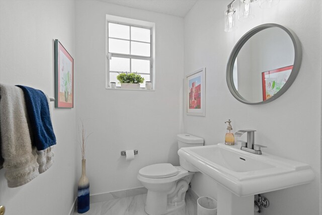 half bathroom featuring toilet, marble finish floor, baseboards, and a sink