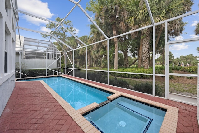 view of pool featuring glass enclosure, a pool with connected hot tub, and a patio