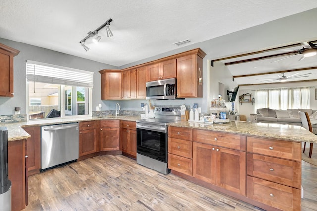 kitchen with light wood-style flooring, brown cabinets, appliances with stainless steel finishes, and a peninsula