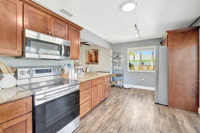 kitchen featuring visible vents, appliances with stainless steel finishes, light wood-style floors, brown cabinetry, and a textured ceiling