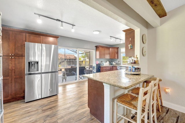 kitchen featuring baseboards, a kitchen bar, a peninsula, light wood-style floors, and stainless steel refrigerator with ice dispenser