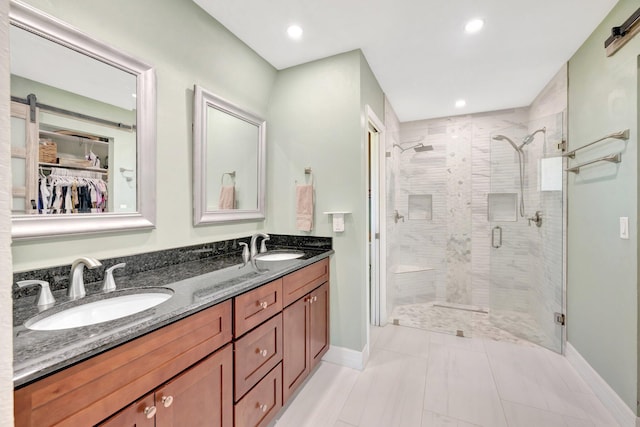 full bathroom with a shower stall, a walk in closet, baseboards, double vanity, and a sink