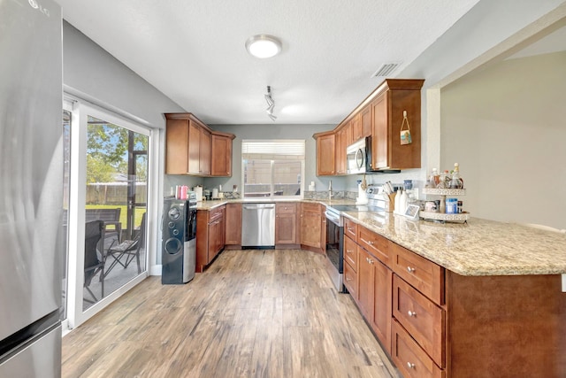 kitchen featuring brown cabinets, light wood-style flooring, light stone counters, a peninsula, and appliances with stainless steel finishes
