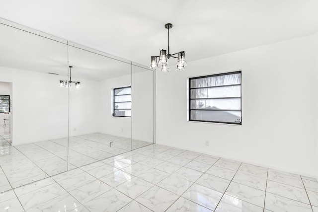 spare room featuring marble finish floor and a notable chandelier