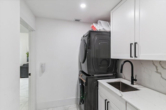 washroom with stacked washer and clothes dryer, marble finish floor, a sink, cabinet space, and baseboards