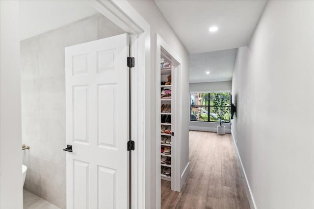 hallway with recessed lighting, a textured ceiling, baseboards, and wood finished floors