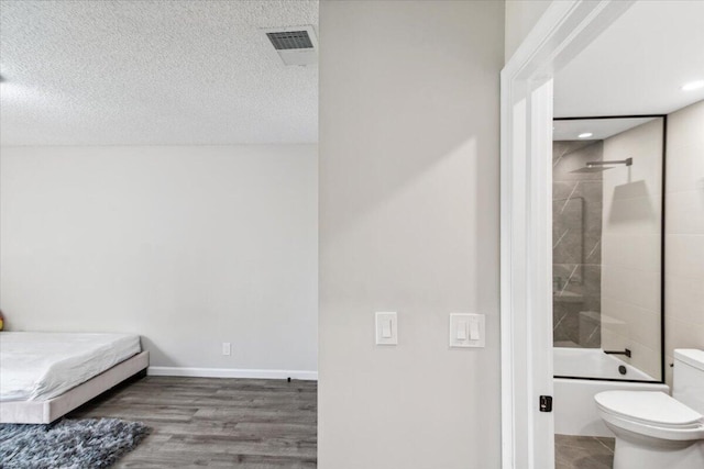 bedroom with baseboards, wood finished floors, visible vents, and a textured ceiling