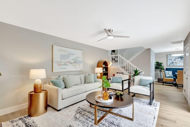 living room featuring stairway, light wood-type flooring, visible vents, and baseboards