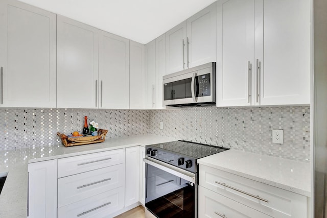 kitchen with light stone counters, stainless steel microwave, backsplash, and electric range oven