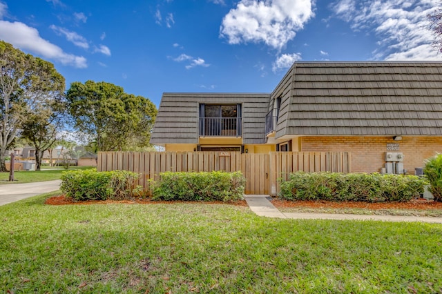 view of front of home with mansard roof, a front yard, fence, and brick siding