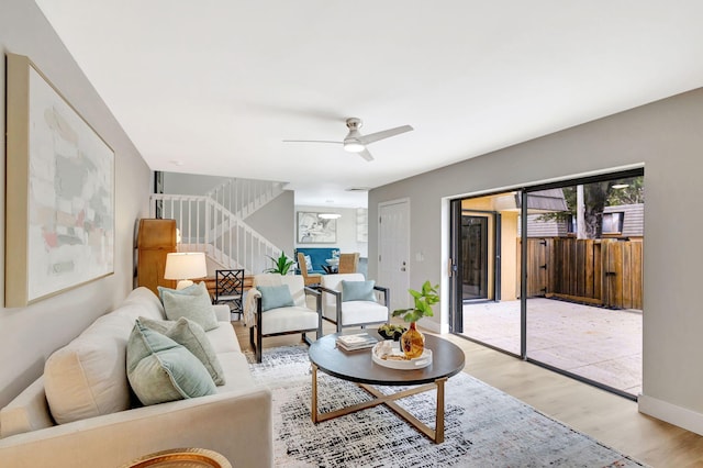 living area featuring light wood finished floors, ceiling fan, stairs, and baseboards