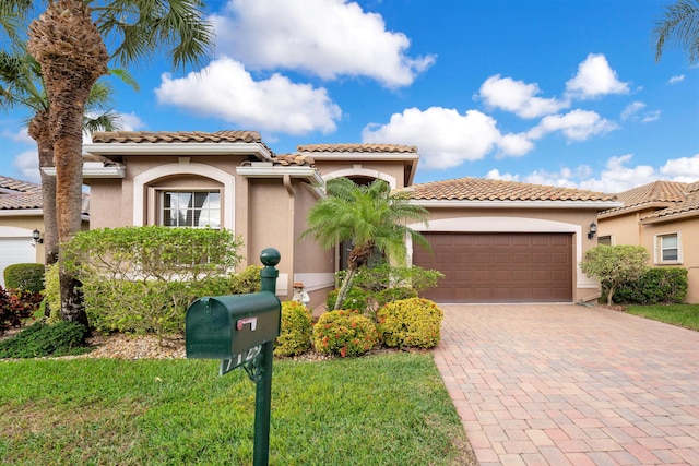 mediterranean / spanish house with decorative driveway, an attached garage, a tile roof, and stucco siding