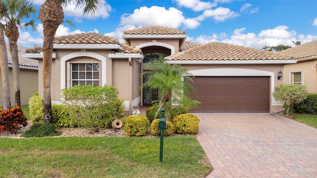 mediterranean / spanish home with a garage, decorative driveway, a tile roof, and stucco siding