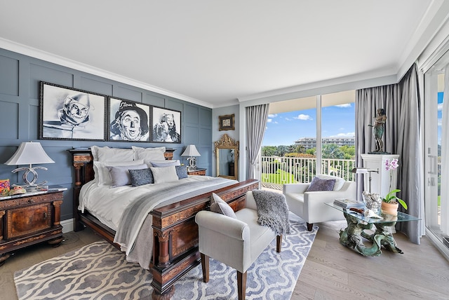 bedroom with access to exterior, crown molding, a decorative wall, and wood finished floors