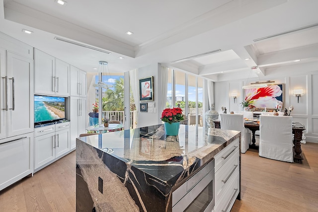 kitchen with stainless steel microwave, ornamental molding, dark stone countertops, light wood-type flooring, and coffered ceiling