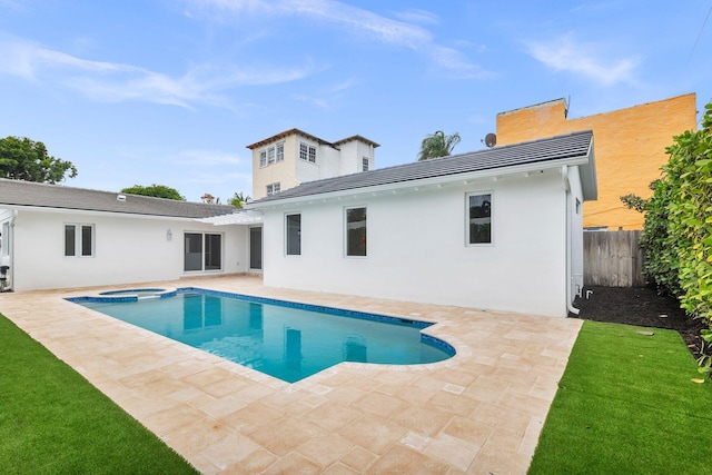 rear view of property featuring a patio area, a pool with connected hot tub, fence, and stucco siding