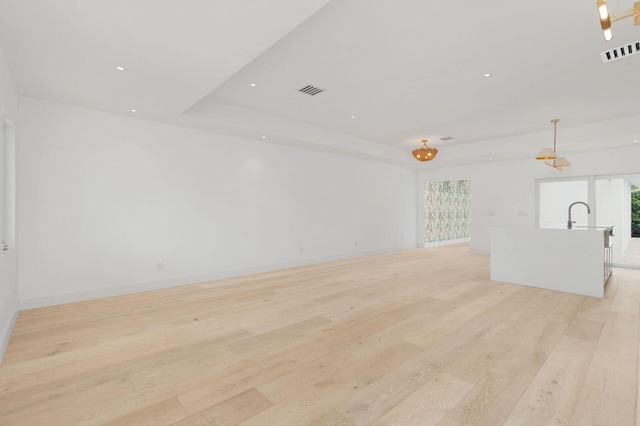 empty room featuring light wood finished floors, a tray ceiling, visible vents, and a sink