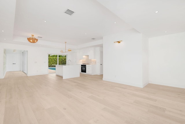 unfurnished living room featuring light wood finished floors, baseboards, visible vents, a tray ceiling, and recessed lighting