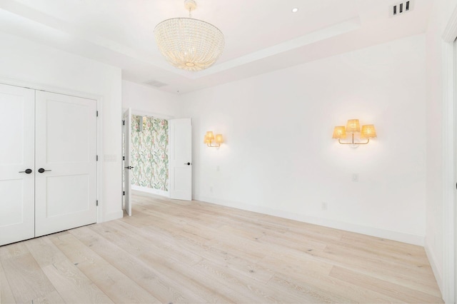 spare room featuring light wood finished floors, baseboards, visible vents, a raised ceiling, and an inviting chandelier